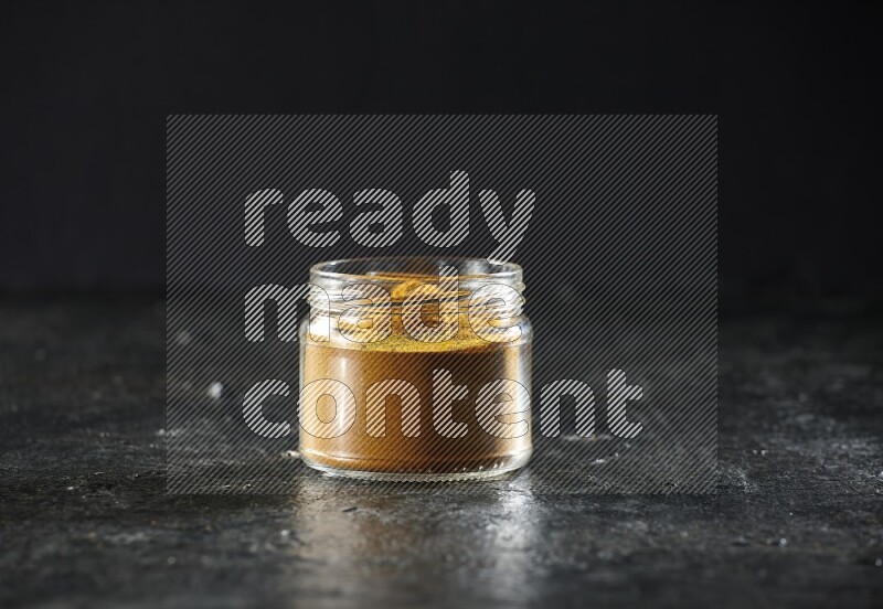 A glass jar full of turmeric powder on a textured black flooring