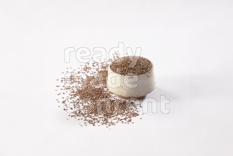A pottery beige bowl full of flax seeds and more seeds spread on a white flooring
