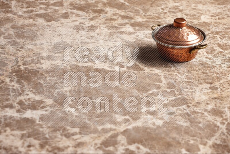 A small copper pot on beige marble background