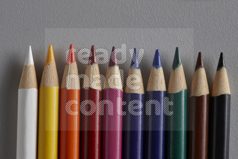 A collection of colored pencils arranged showcasing a gradient of different hues on grey background