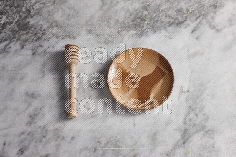 Multicolored pottery plate with wooden honey dipper on the side on grey marble background