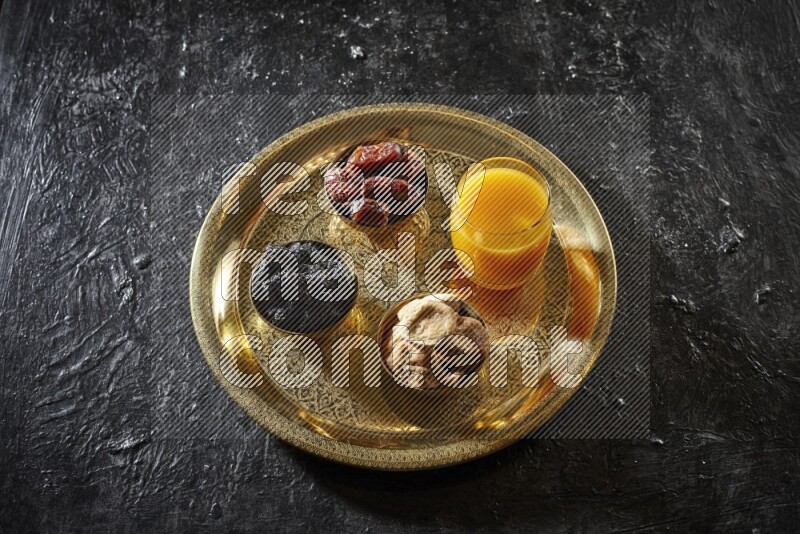 Dried fruits in metal bowls with qamar eldin on a tray in dark setup