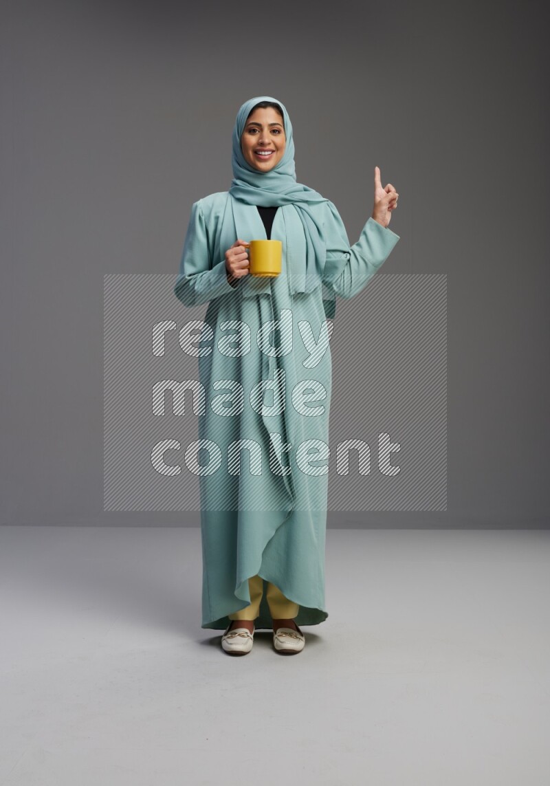 Saudi Woman wearing Abaya standing  holding a mug on Gray background