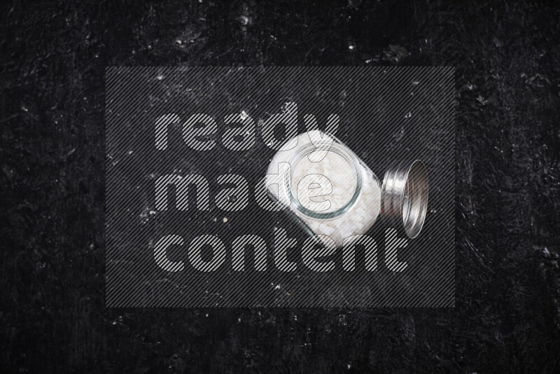 A glass jar full of coarse sea salt crystals on black background