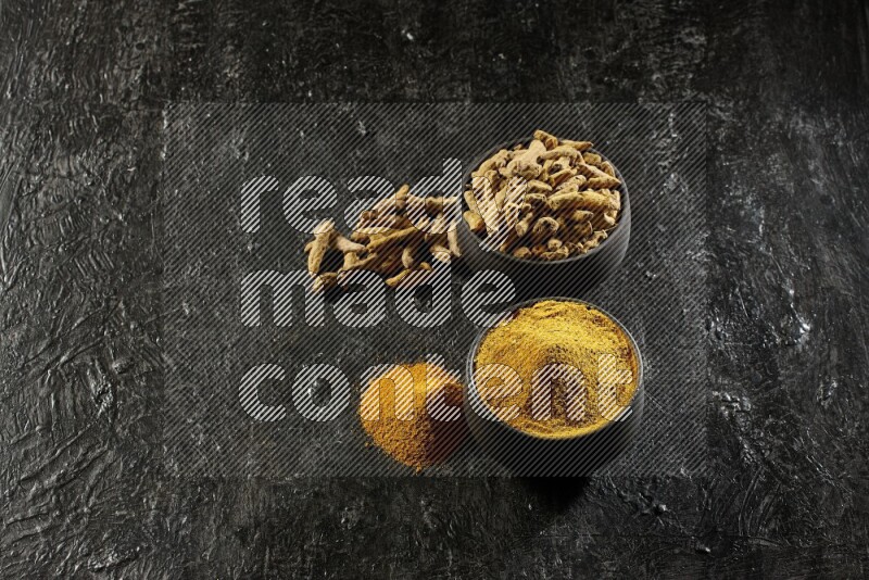 وعاءان من الفخار باللون الأسود، أحدهما ممتلئ ببودرة الكركم والآخر ممتلئ بأصابع كاملة من الكركم المجفف على خلفية سوداء