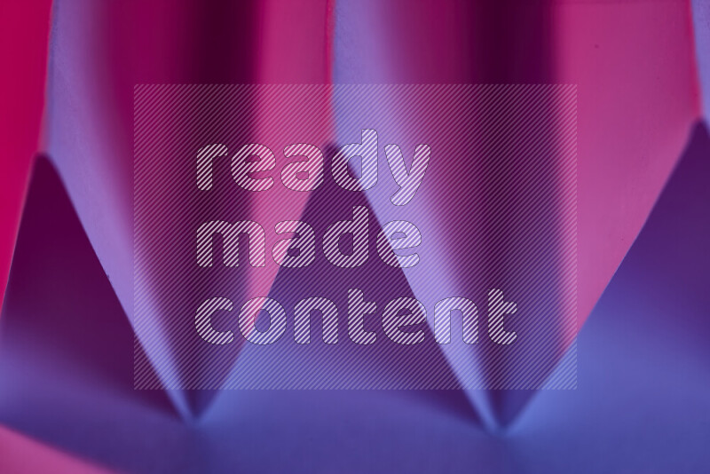 A close-up abstract image showing sharp geometric paper folds in blue and pink gradients