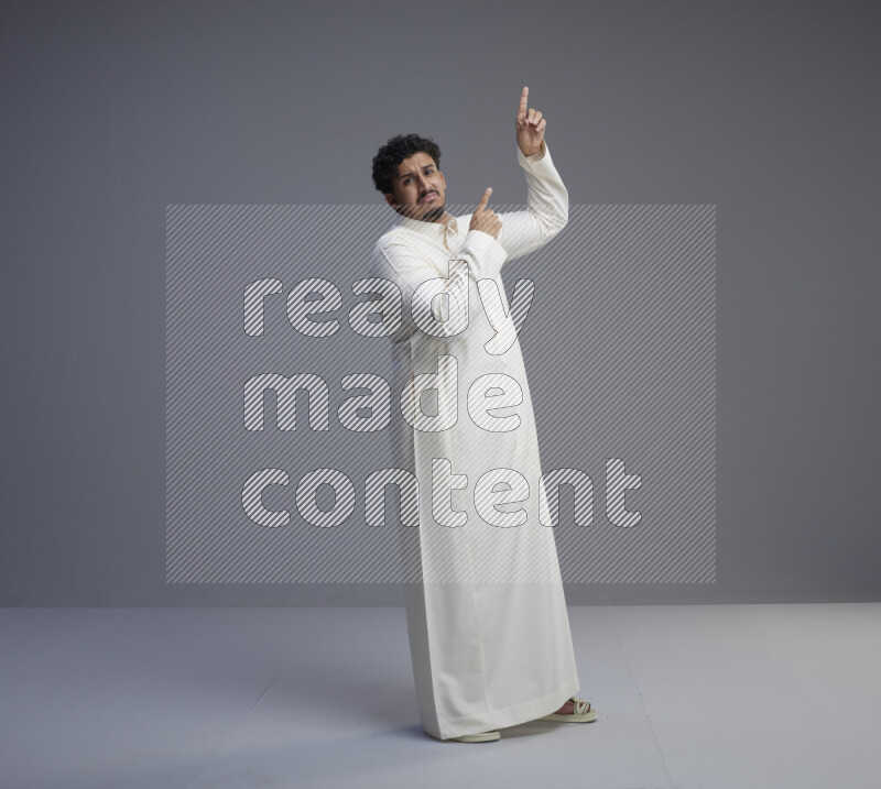 A Saudi man standing wearing thob interacting with the camera on gray background