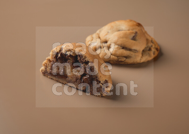 a chocolate chip cookie with another one cut in half on a brown background