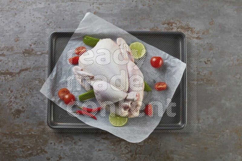 whole raw chicken on an oven trey direct on a rustic grey background