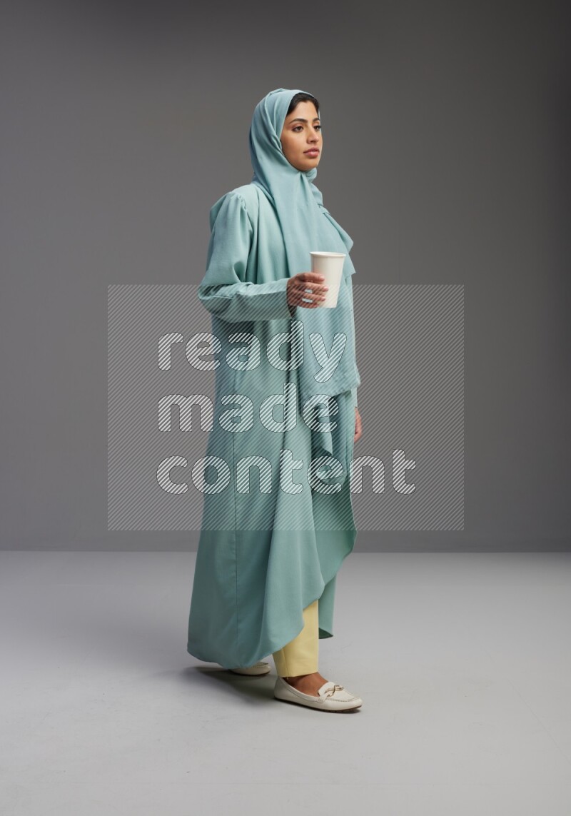 Saudi Woman wearing Abaya standing  holding paper cup on Gray background