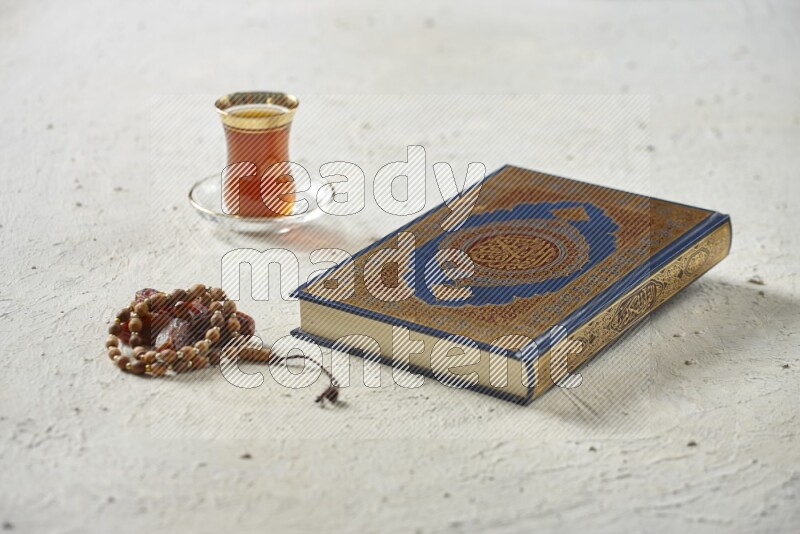 Quran with dates, prayer beads and different drinks all placed on textured white background