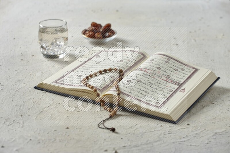 Quran with dates, prayer beads and different drinks all placed on textured white background
