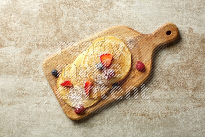 Three stacked mixed berries pancakes on a wooden board on beige background
