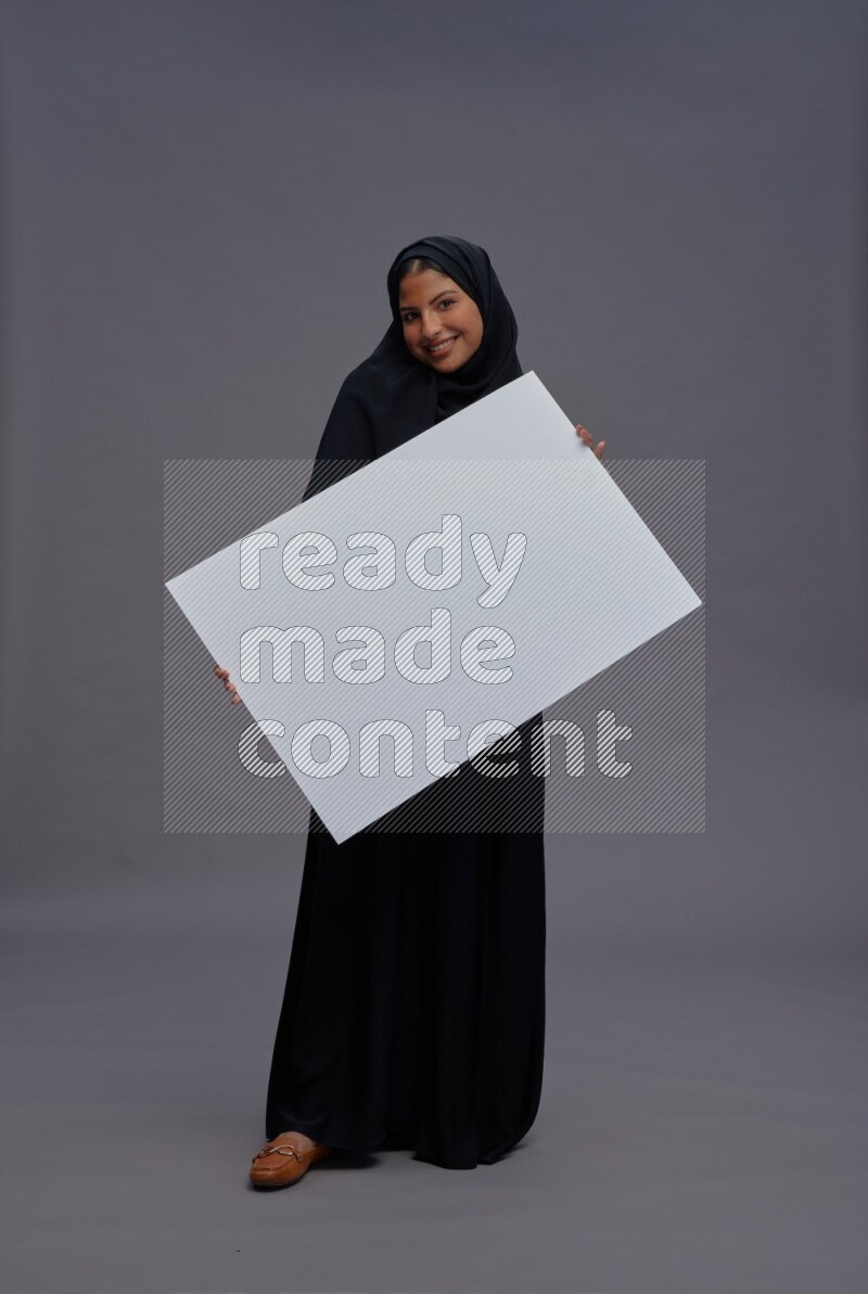 Saudi woman wearing Abaya standing holding white board on gray background