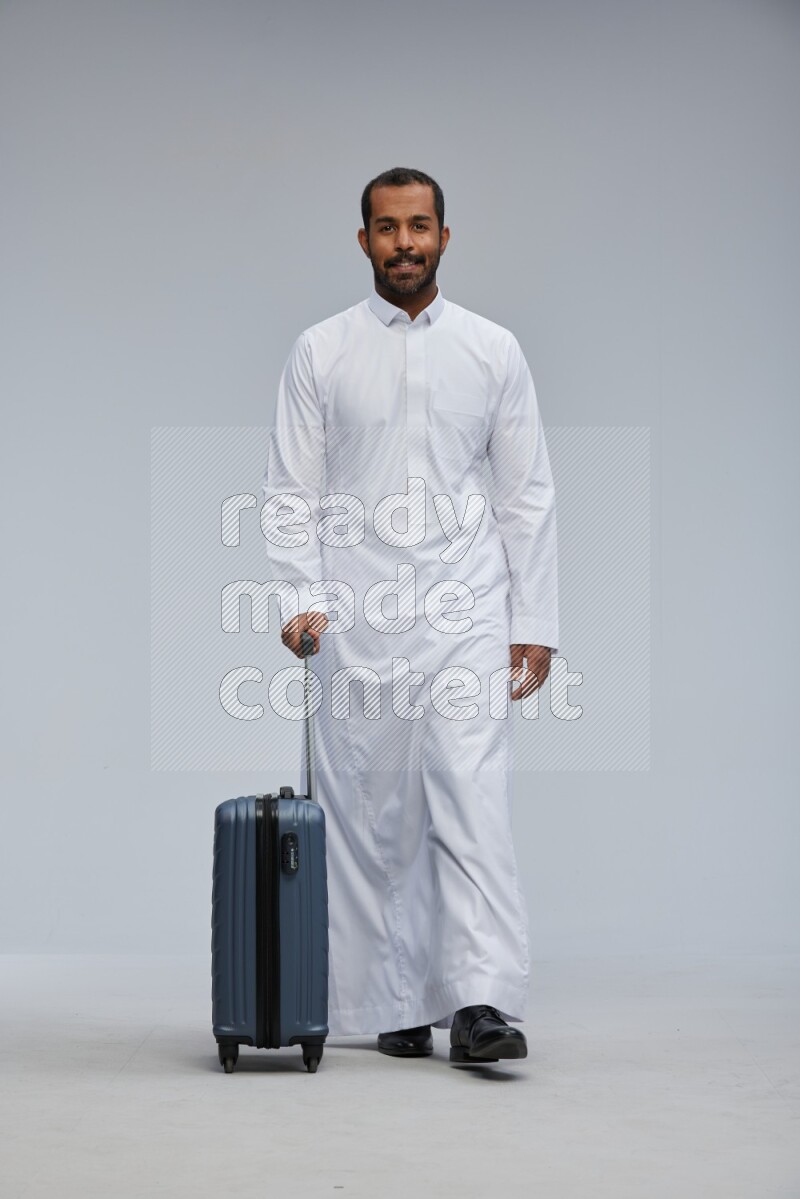 Saudi man wearing thob standing holding Travel bag on Gray background