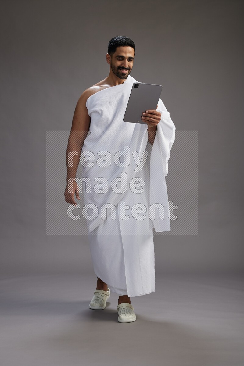 A man wearing Ehram and holding a tablet on gray background