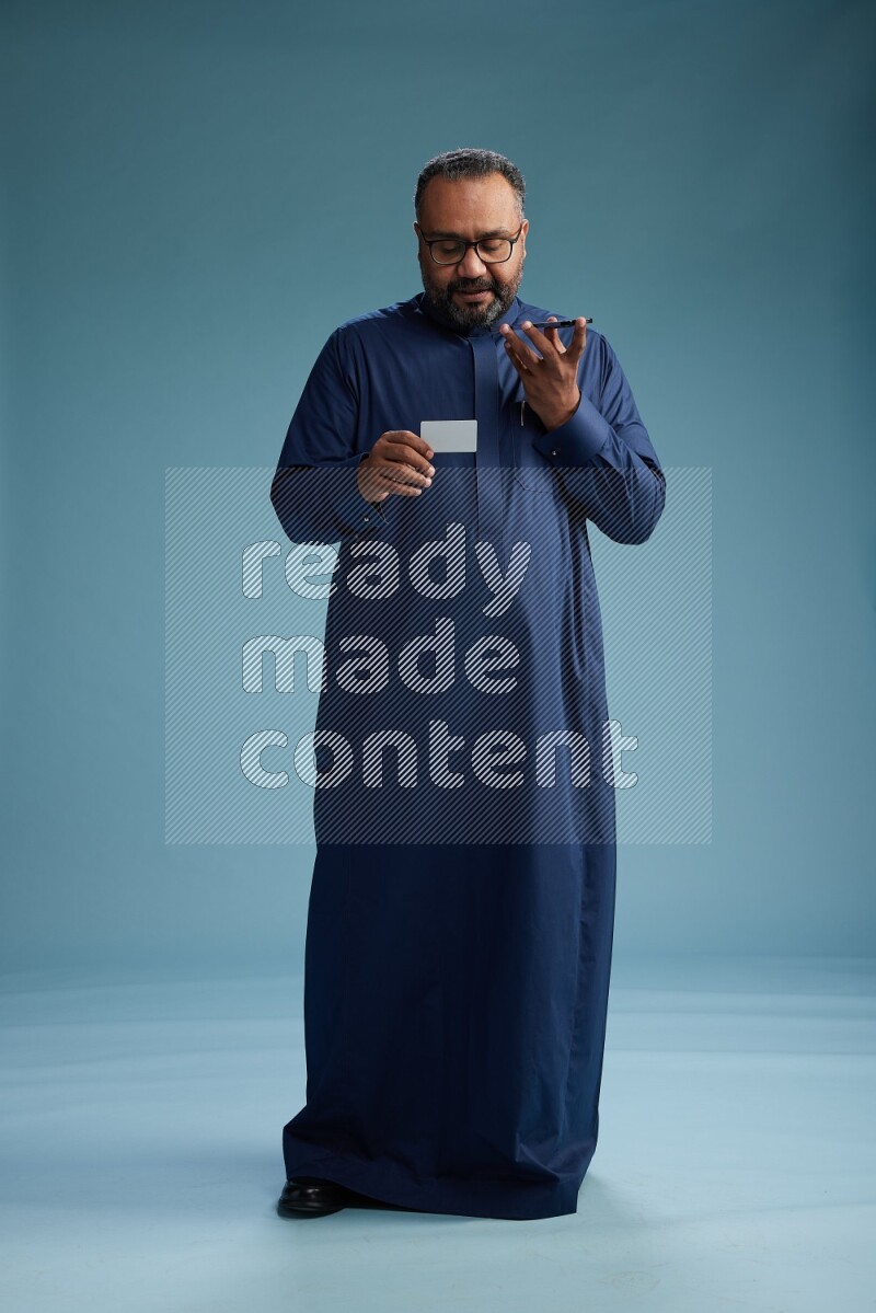 Saudi Man without shimag Standing holding ATM while talking on phone on blue background