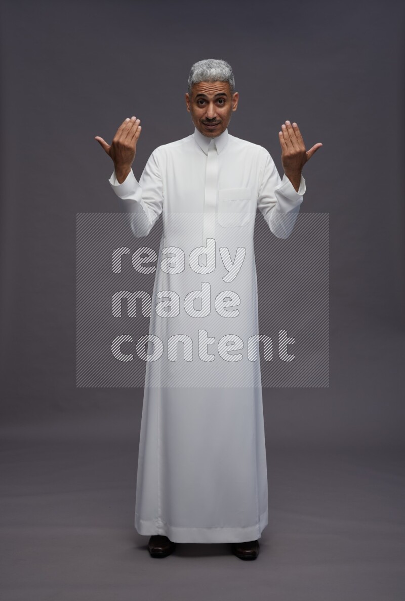 Saudi man wearing thob standing interacting with the camera on gray background