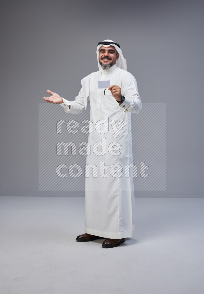 Saudi man Wearing Thob and white Shomag standing holding ATM card on Gray background