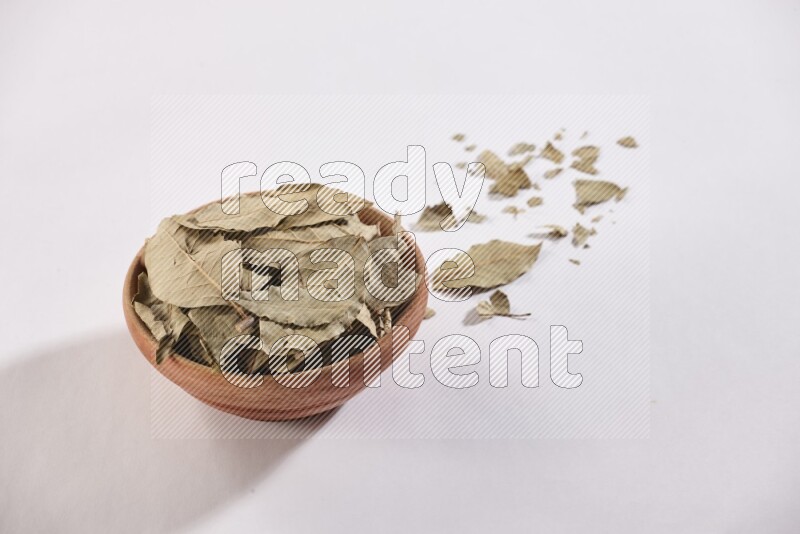 A wooden bowl filled with dried bay leaves on white flooring in different angles