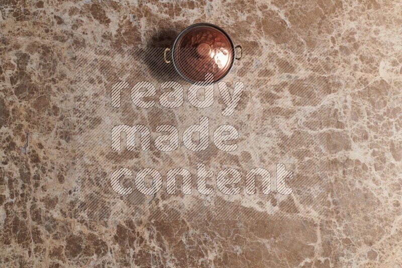A small copper pot on beige marble background