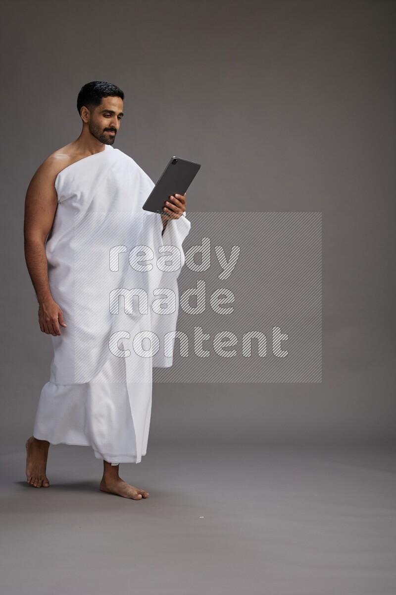 A man wearing Ehram and holding a tablet on gray background
