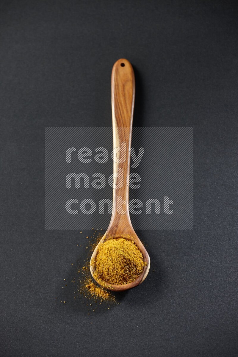A wooden ladle full of turmeric powder on black flooring