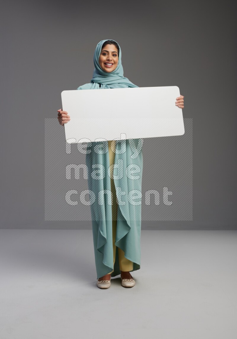 Saudi Woman wearing Abaya standing holding board on Gray background