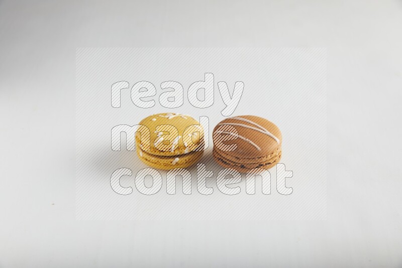 45º Shot of of two assorted Brown Irish Cream, and Yellow Piña Colada macarons on white background
