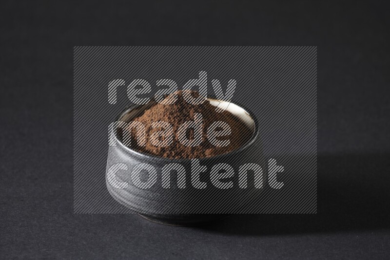 A black pottery bowl full of cloves powder on a black flooring