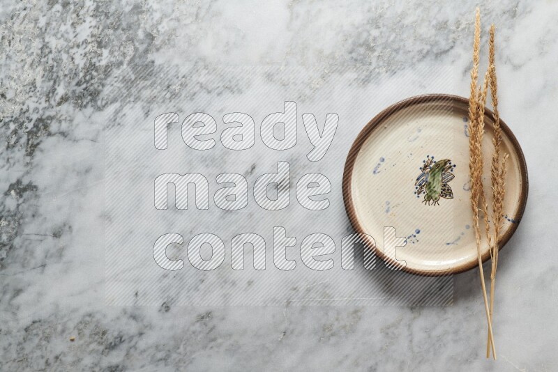 Wheat stalks on decorative pottery plate on grey marble background