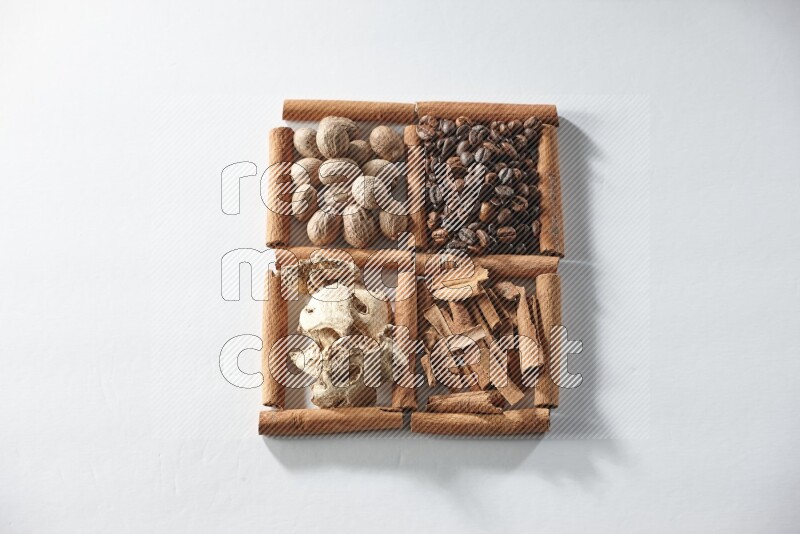 4 مربعات من أعواد القرفة ممتلئة بحبوب القهوة وجوزة الطيب والقرفة والزنجبيل المجفف على أرضية بيضاء