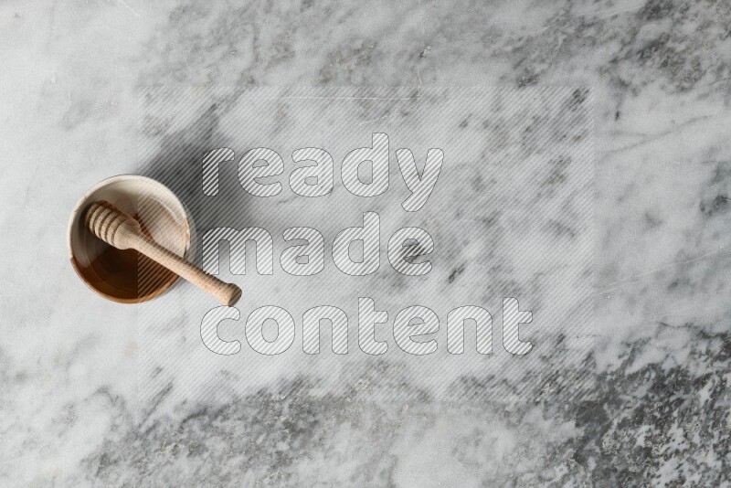 Multicolored pottery bowl with wooden honey dipper in it on grey marble background