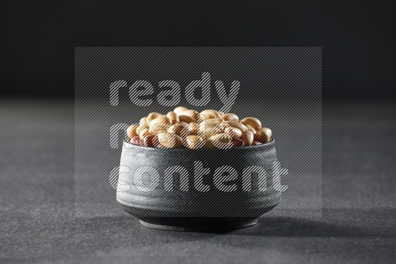 A black pottery bowl full of peeled peanuts on a black background in different angles