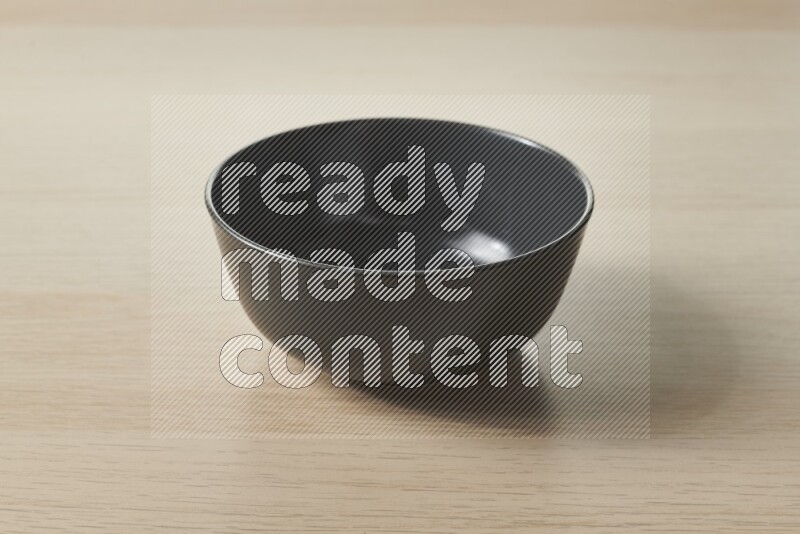 A black ceramic bowl on light wooden background