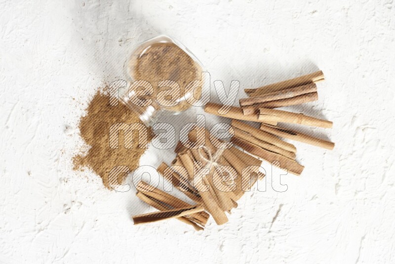 Flipped herbs glass jar full of cinnamon powder and cinnamon sticks in the back on a textured white background