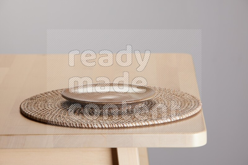 multi-colored pottery Plate placed on a big light colored straw placemat on the edge of wooden table