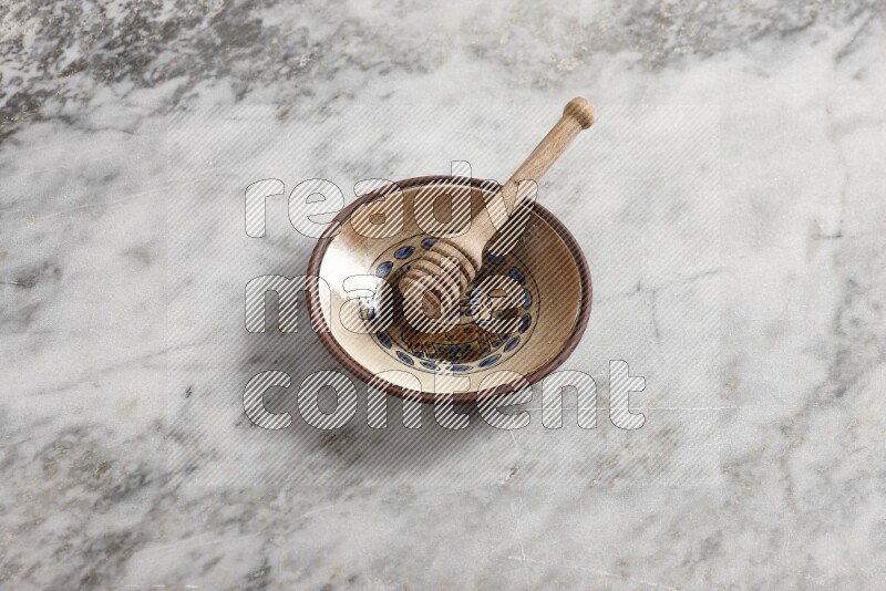 Decorative pottery plate with wooden honey dipper in it on grey marble background