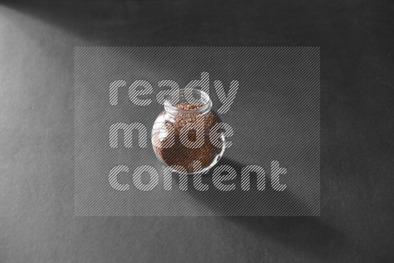 A glass spice jar full of flax on black flooring