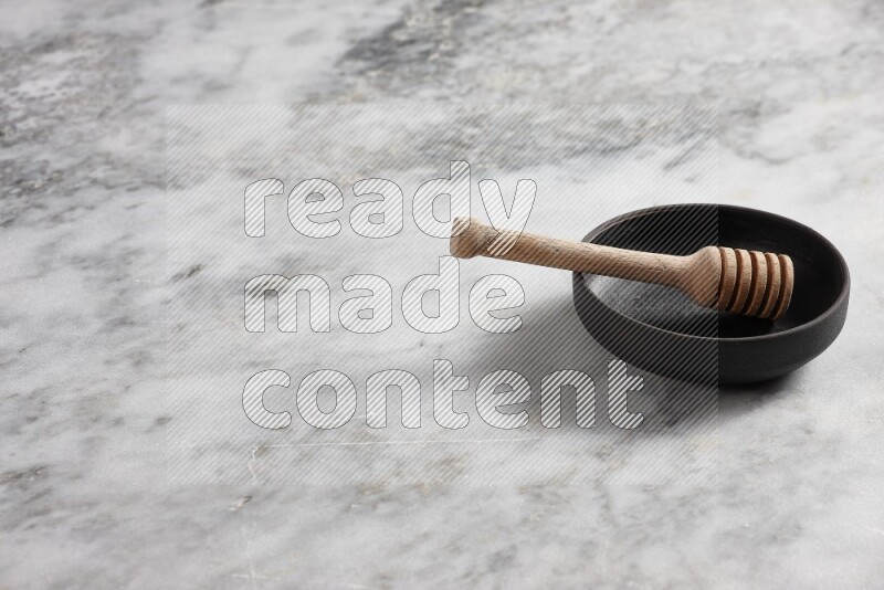 Black pottery bowl with wooden honey dipper in it on grey marble background