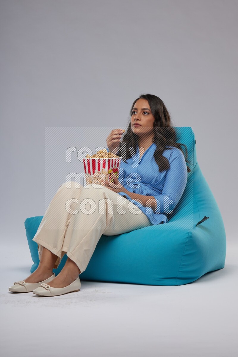 A woman sitting on a blue beanbag and eating popcorn