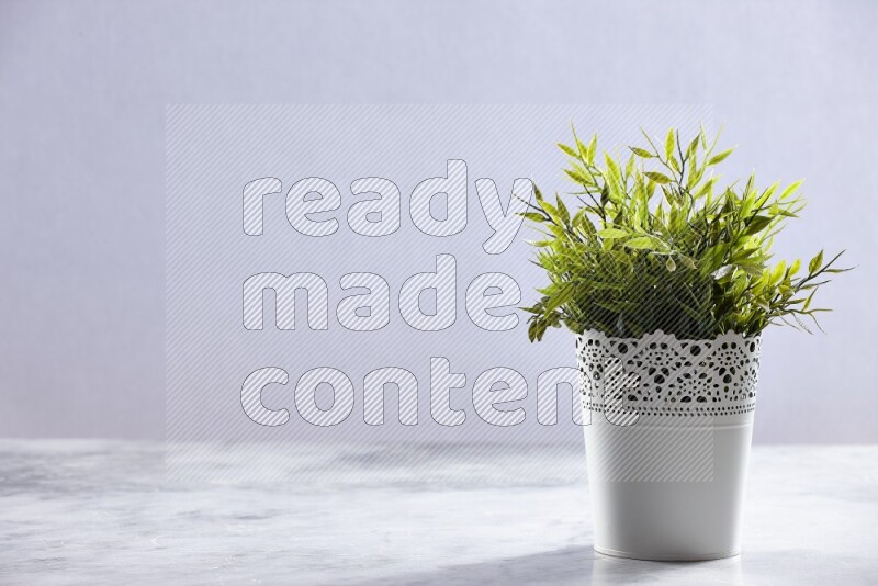 Green artificial plant in white decorative pot on grey marble background