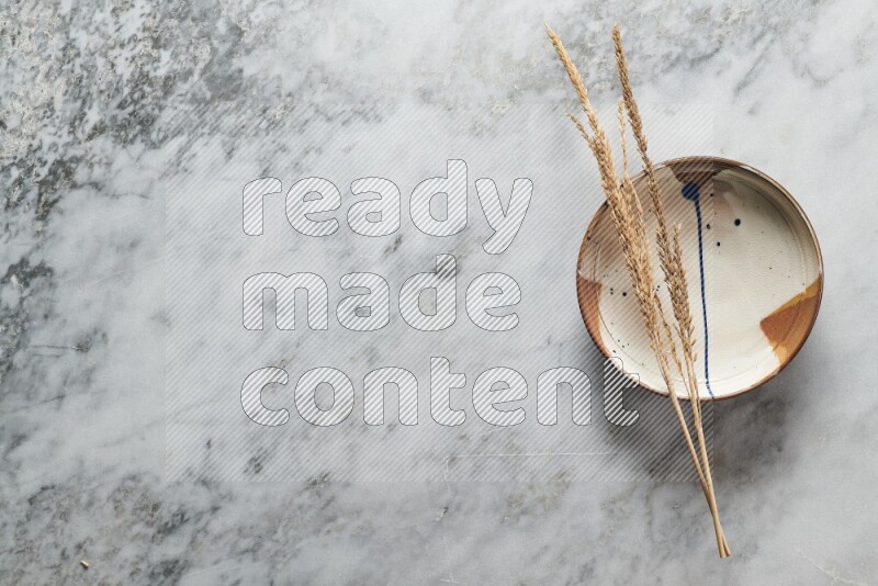 Wheat stalks on multicolored pottery plate on grey marble background