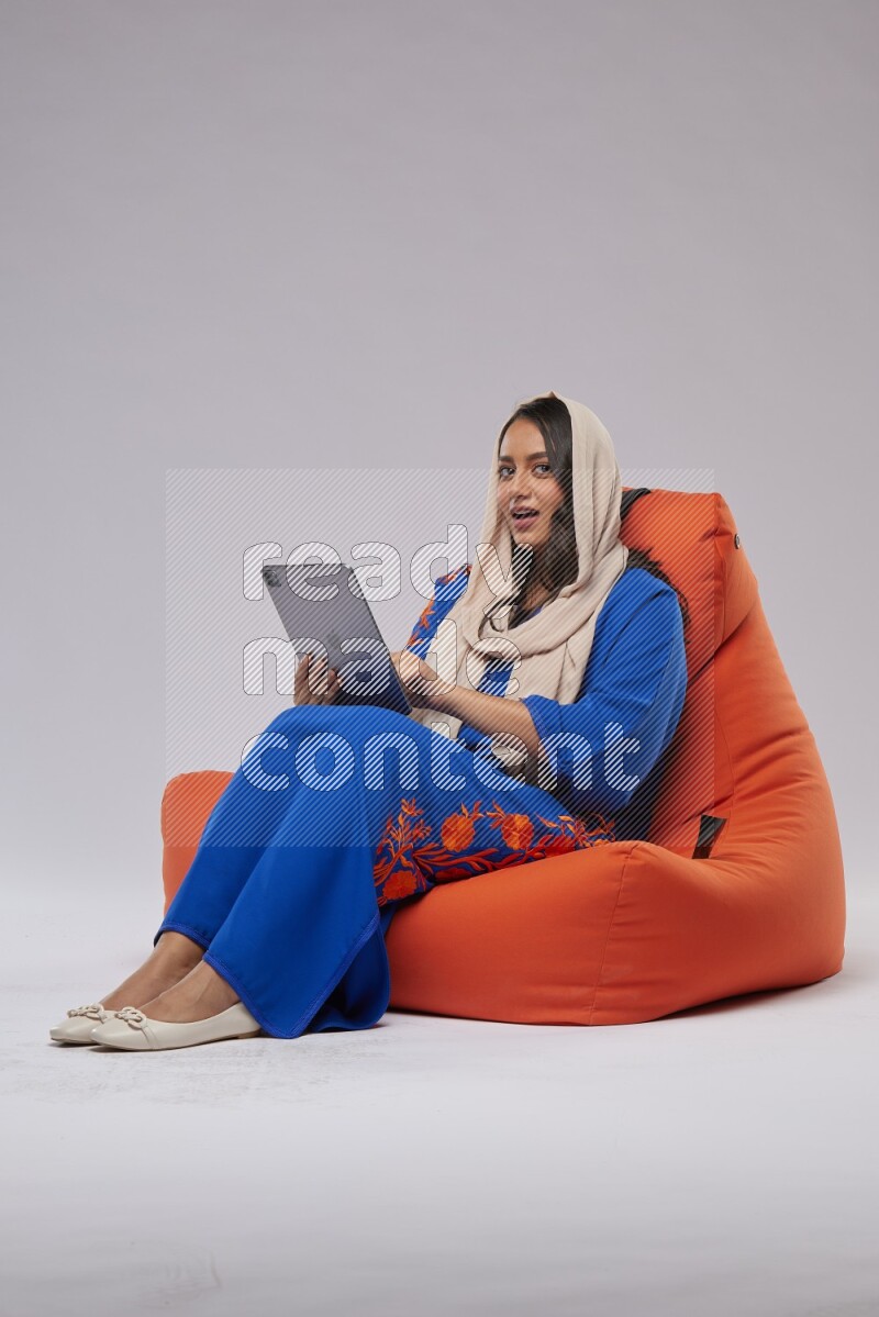 A Saudi woman sitting on an orange beanbag and working on tablet
