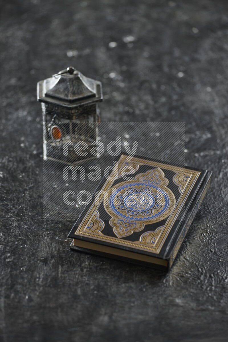 A silver lantern with different drinks, dates, nuts, prayer beads and quran on textured black background