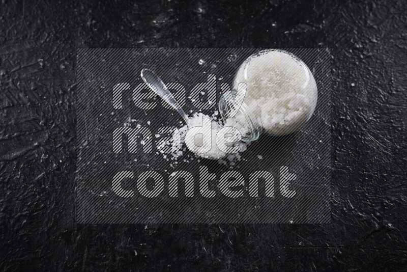 A glass jar full of coarse sea salt crystals on black background