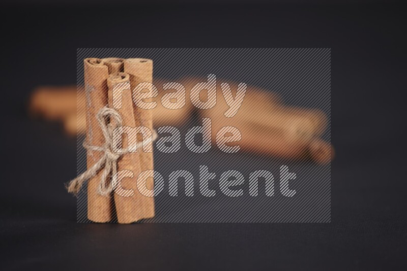4 Cinnamon sticks stacked and bounded with more sticks in the background on black flooring