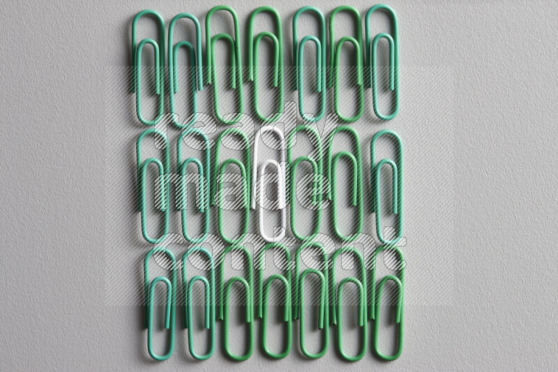 A bunch of green paper clips with a different colored paper clip in the center on grey background