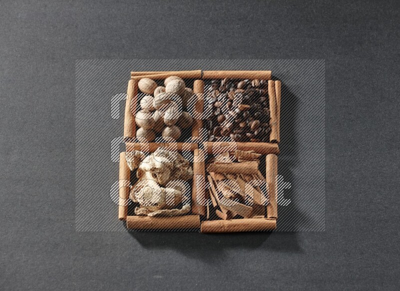 4 مربعات من عيدان القرفة ممتلئة بحبوب القهوة وقطع القرفة والزجبيل المجفف وجوزة الطيب على أرضية سوداء