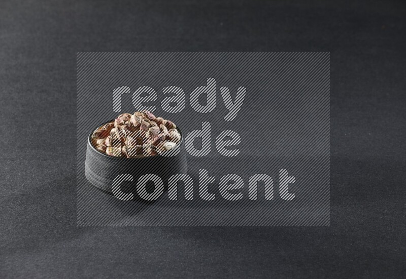 A black pottery bowl full of peeled pistachios on a black background in different angles